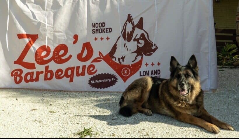 Zee, the German Shepherd that Zee's Barbeque is named after, in front of the banner